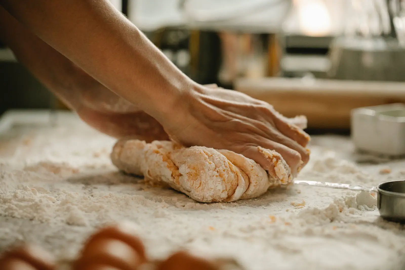 Hands pressing the dough into the floured table, a bright kitchen blurred behind.