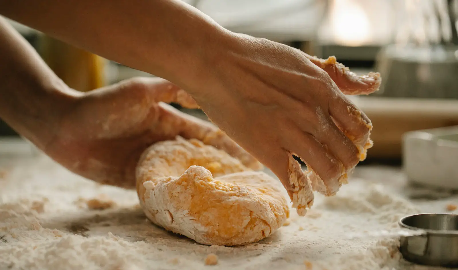 Hands folding the dough over on a floured wooden table.