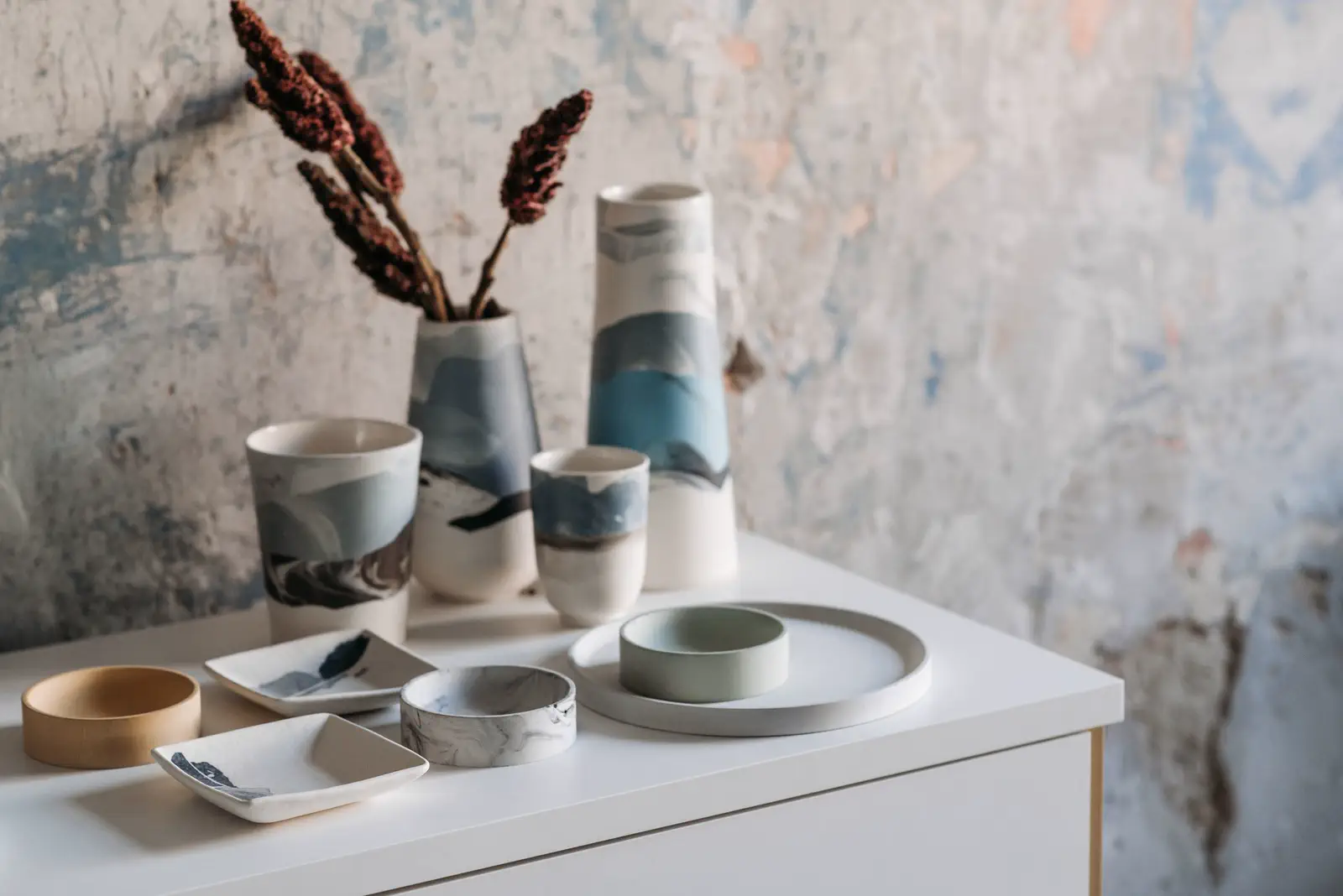 Marbled blue-and-white vases, cups and small dishes with dried flowers against a peeling plaster wall.