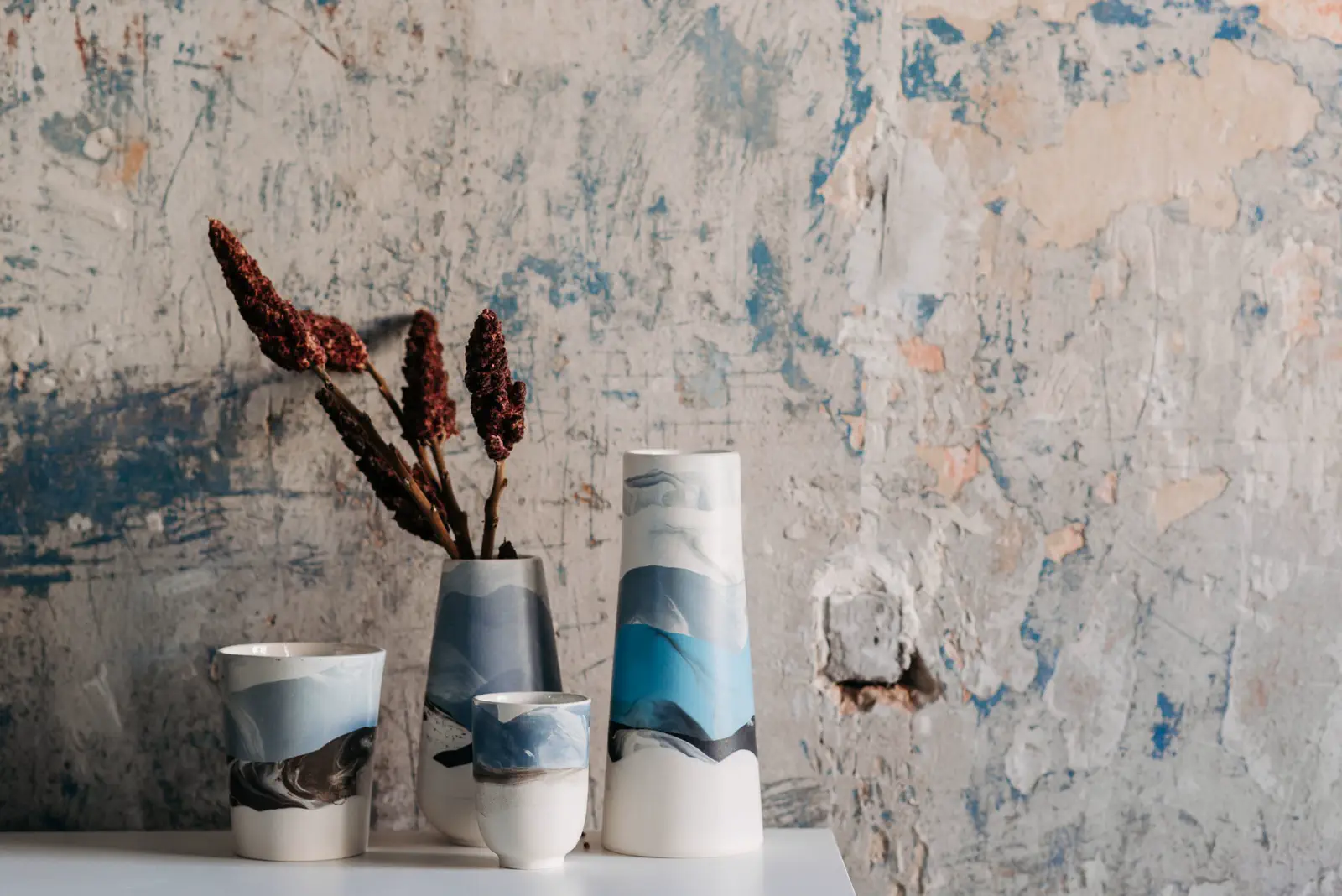 Marbled vases with dried flower stems on a white shelf against the plaster wall.