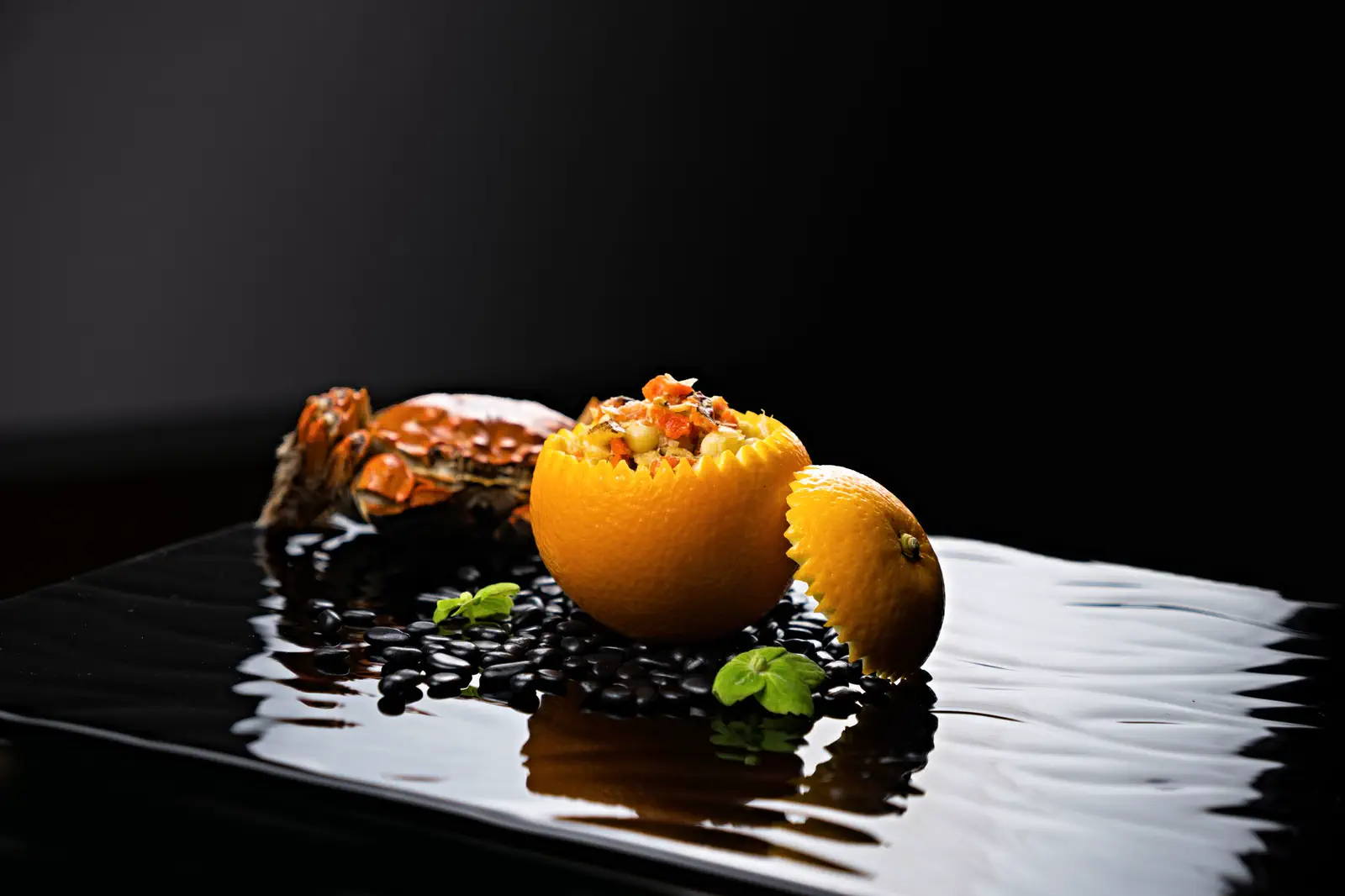 The crab and filled orange on wet black slate, lit hard from the side.