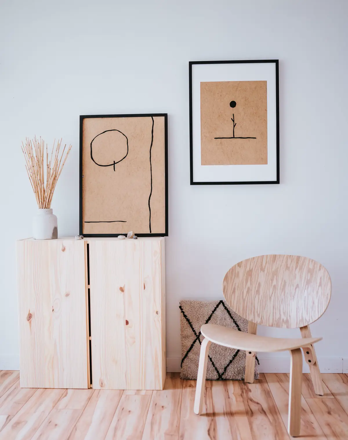 The pine cabinet with two framed prints leaning on it and the plywood chair beside a wool cushion.