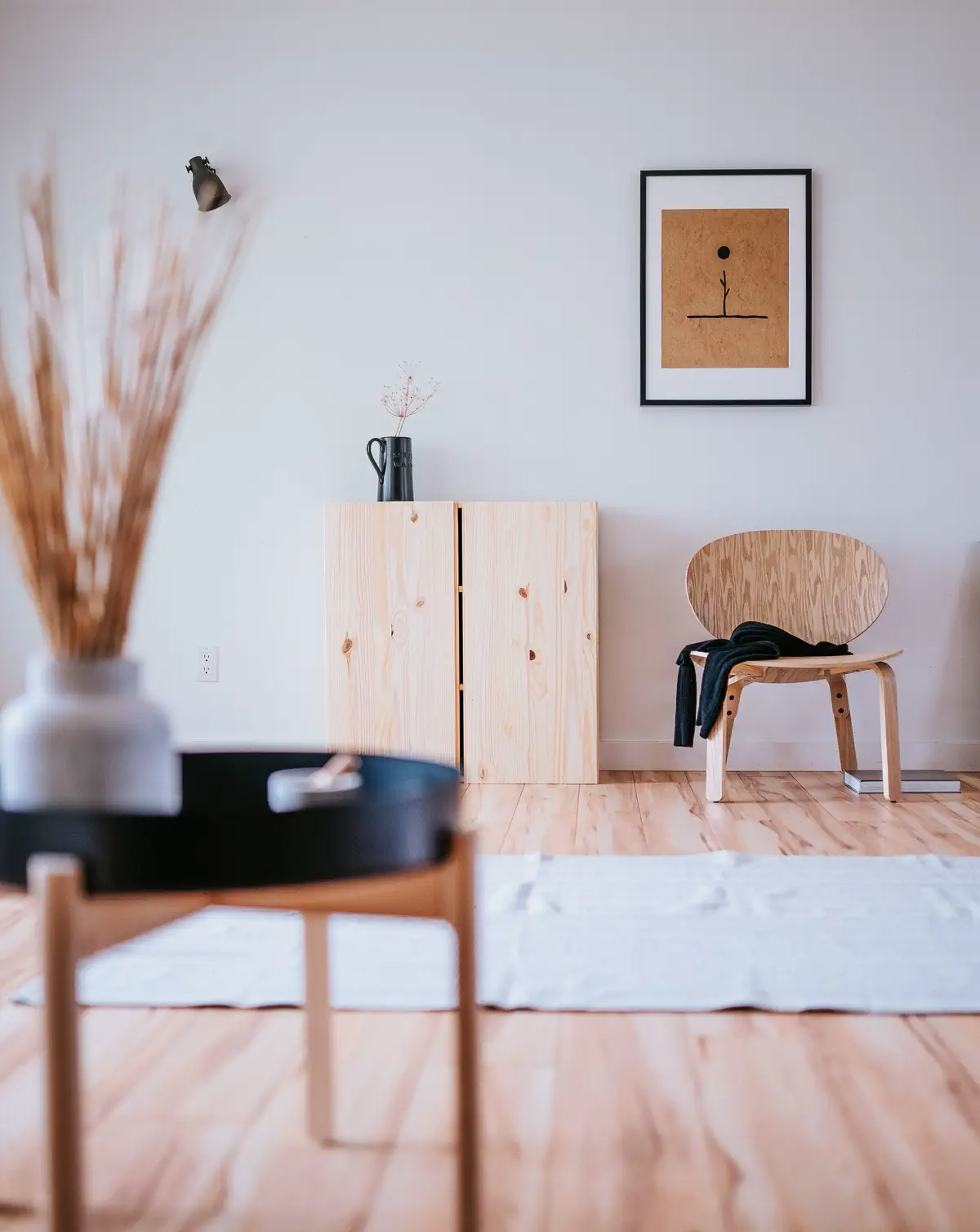 A black tray table in the foreground with the pine cabinet and plywood chair beyond.