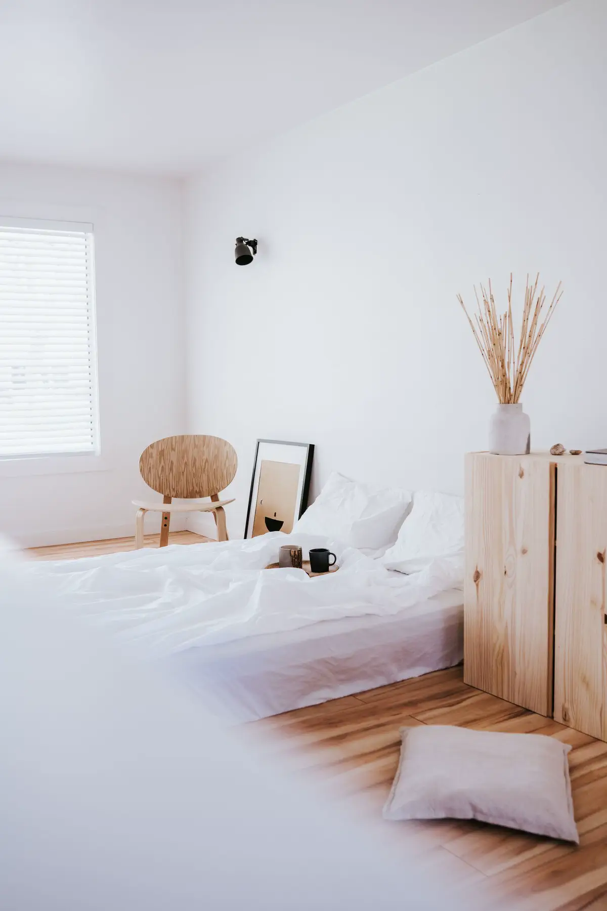 A bright bedroom with a low white bed, the plywood chair and the pine cabinet.