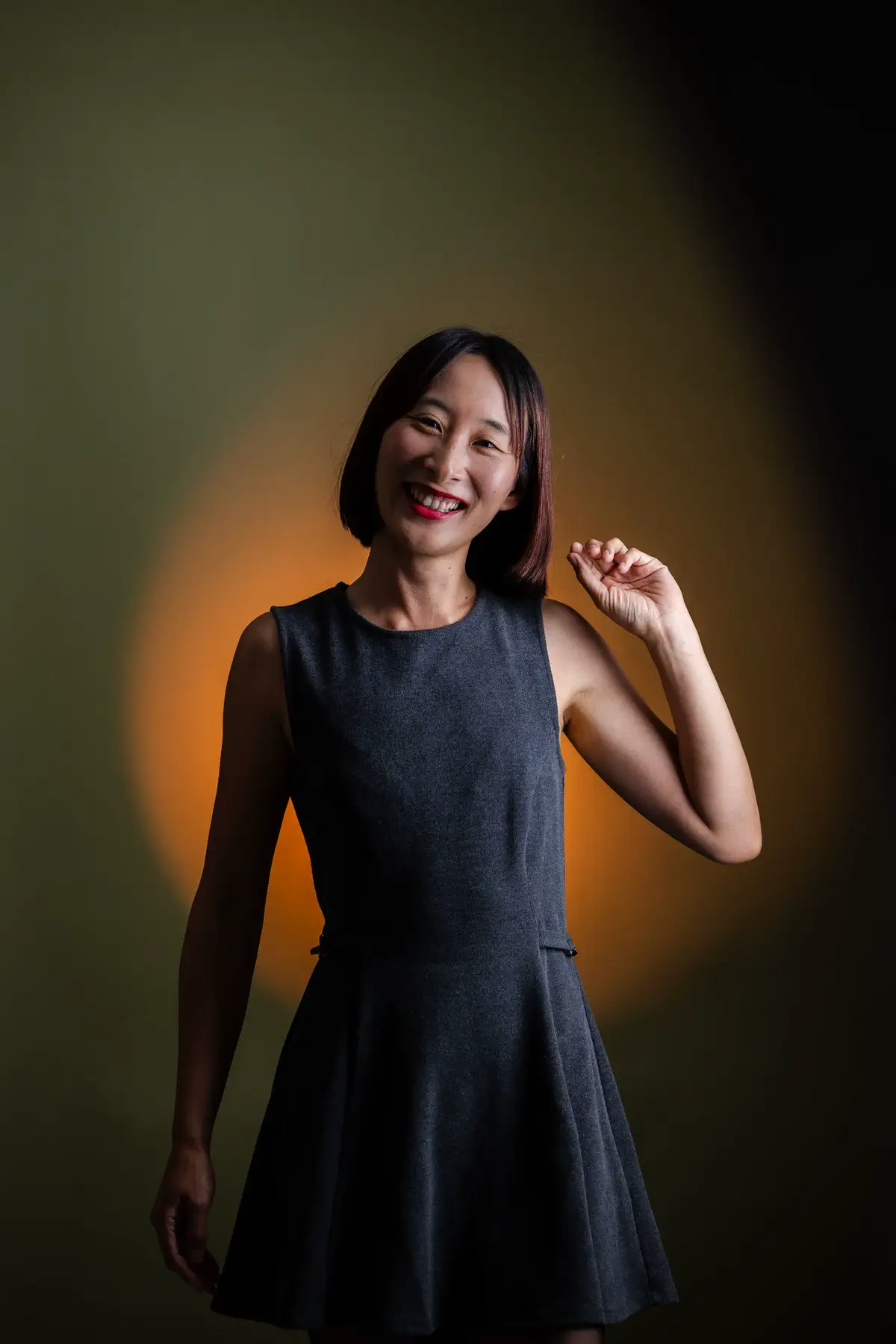 The woman laughing with one hand raised, a warm pool of light on the olive backdrop behind her.