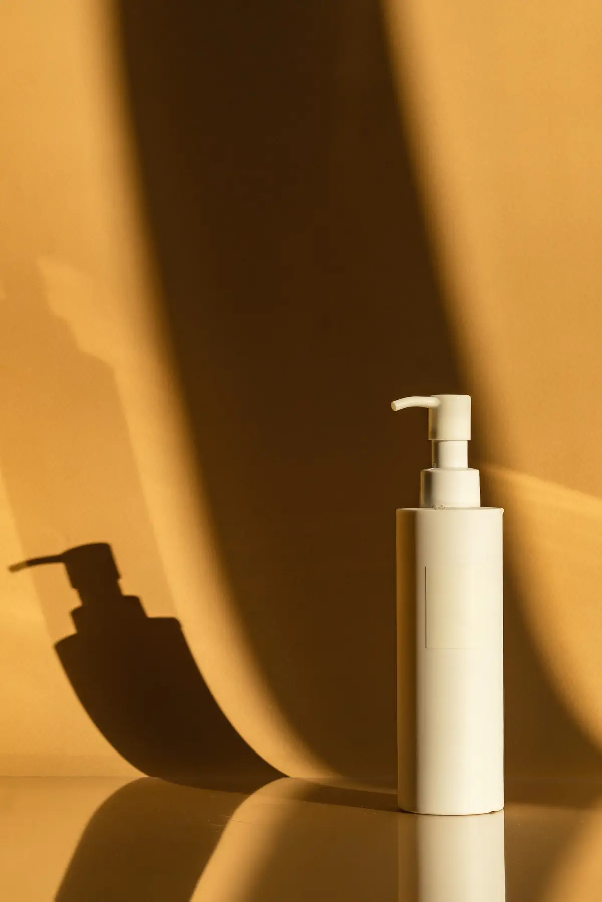 The bottle on a glossy surface against amber cloth striped with curtain shadows.