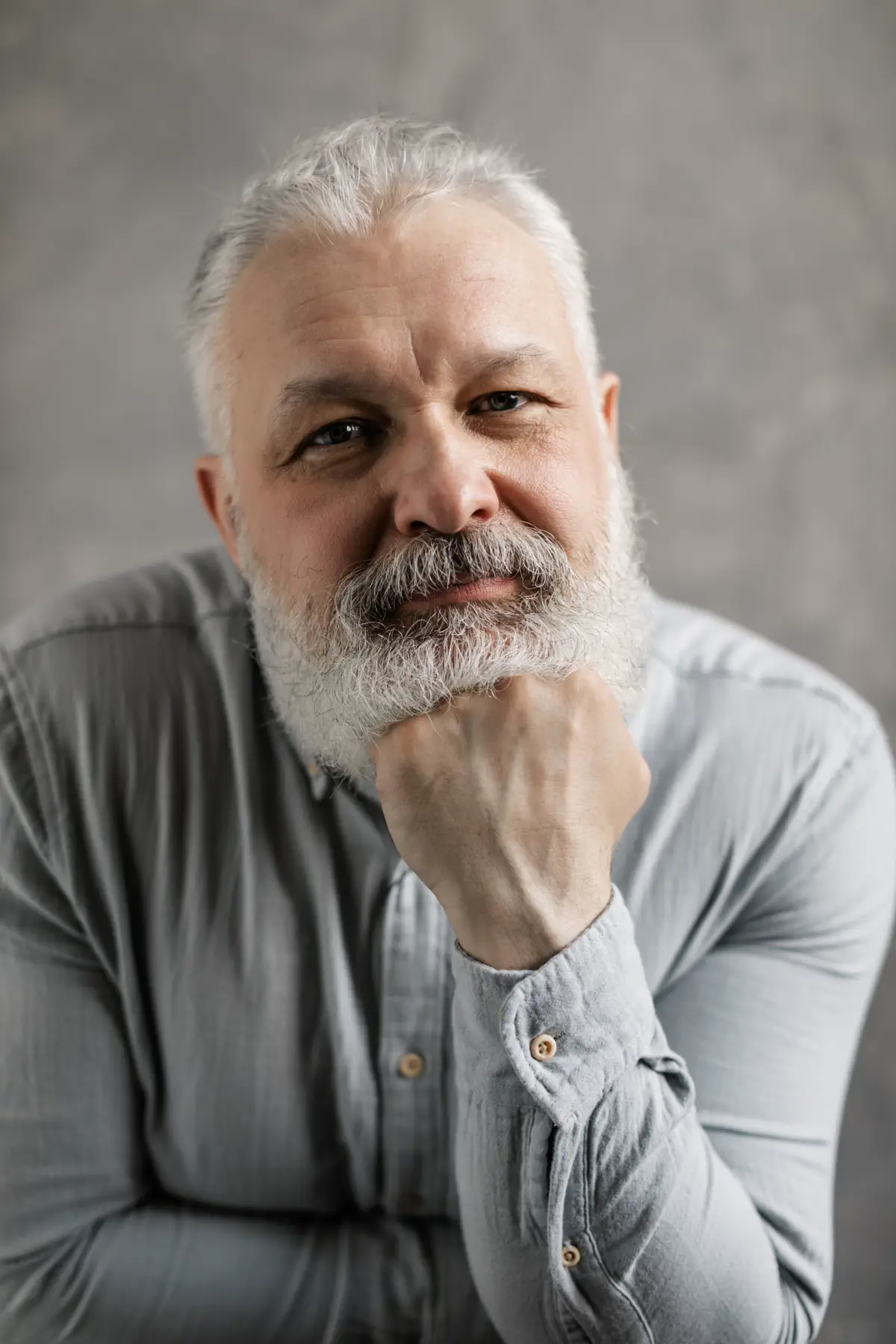 The bearded man resting his chin on his fist, looking straight at the camera.