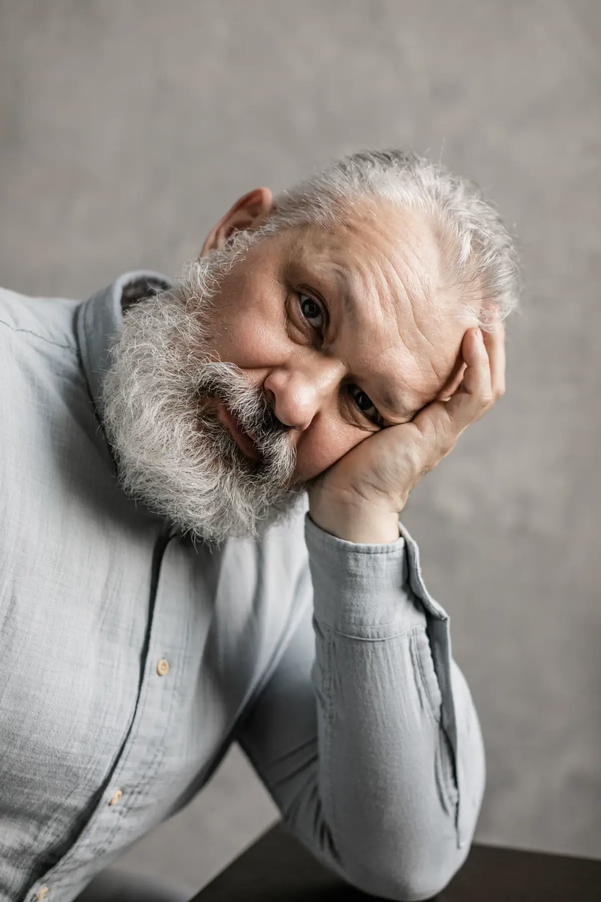 The bearded man leaning on a table with his head resting on his hand.