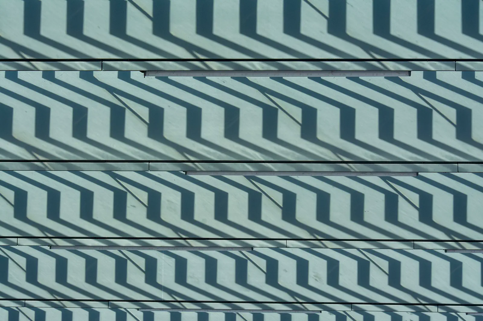 Zig-zag shadows of stair treads across a pale green panelled wall.