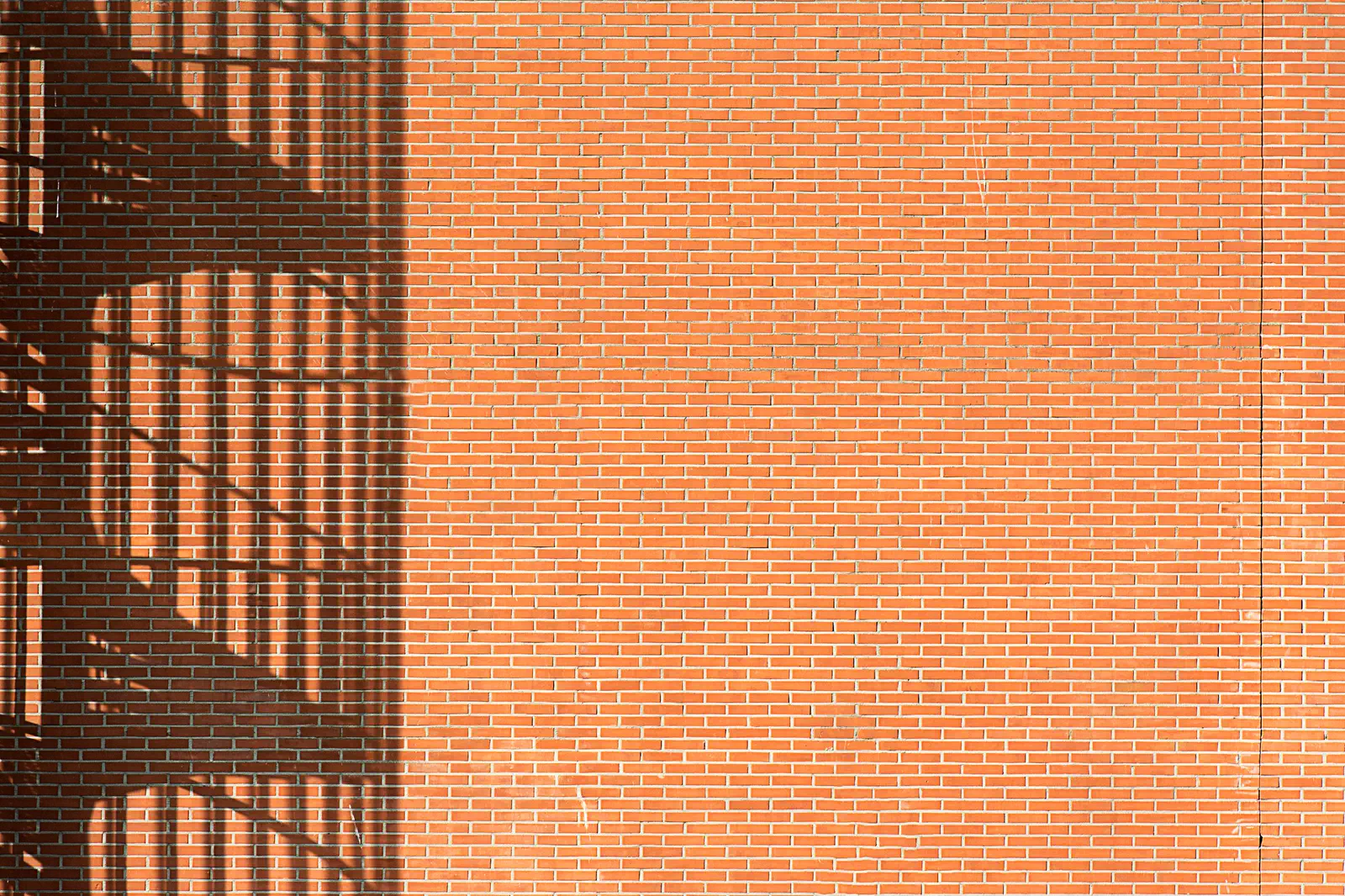 The shadow of an external stair falling across an orange brick wall.