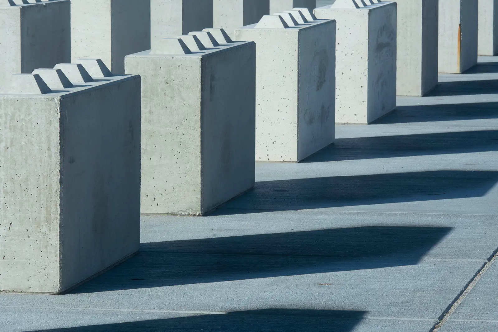 A row of concrete blocks casting long hard shadows on paving.