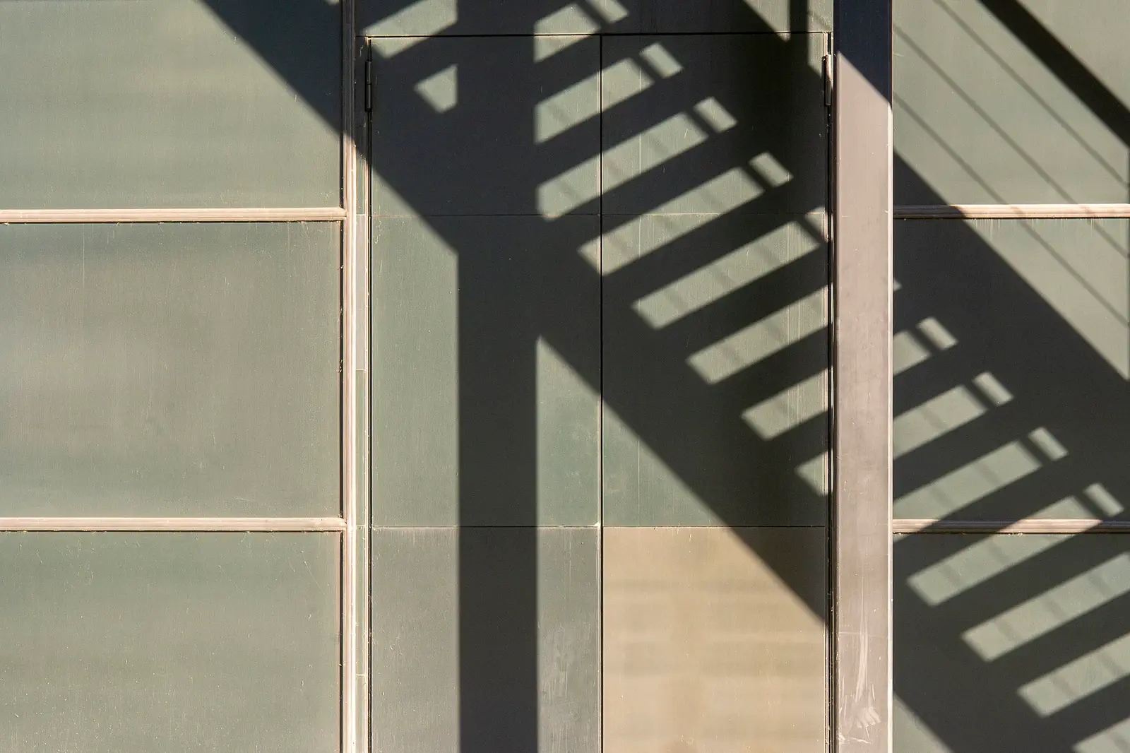 The shadow of a railing on green and sand-coloured panels.