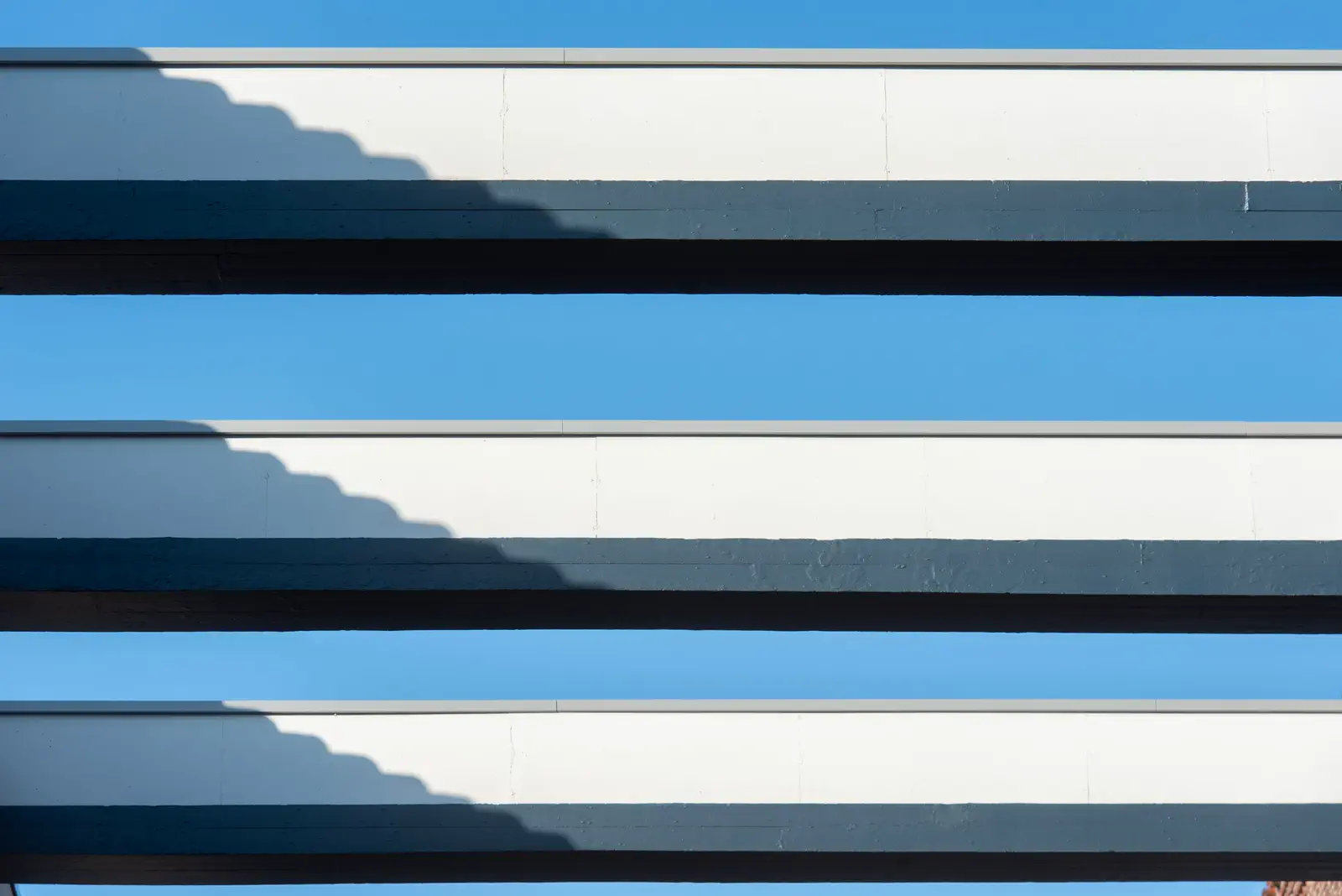Concrete balconies and their stepped shadows against a clear blue sky.