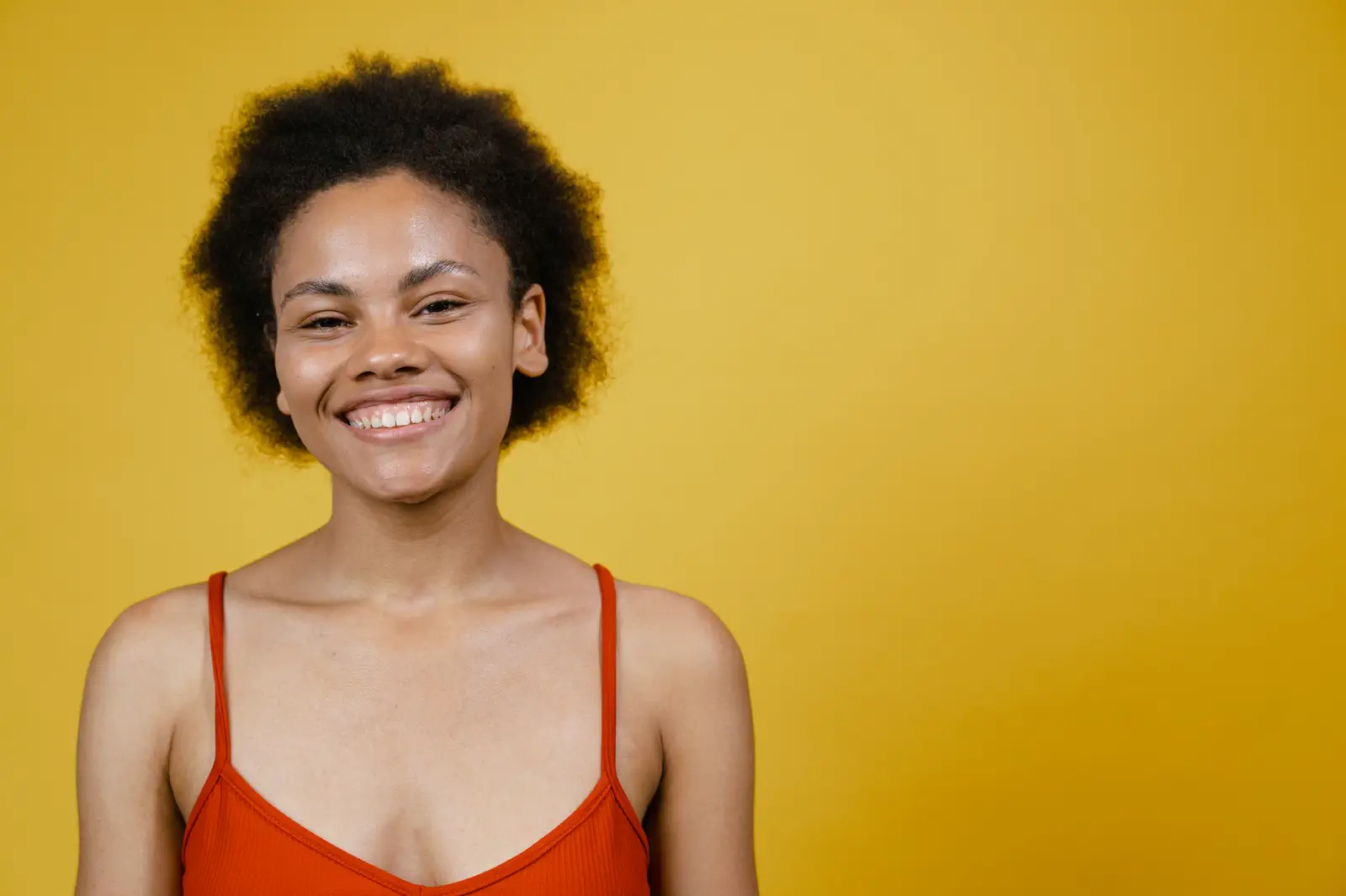 Close portrait of the same smiling sitter in a red-orange camisole against a mustard-yellow backdrop.