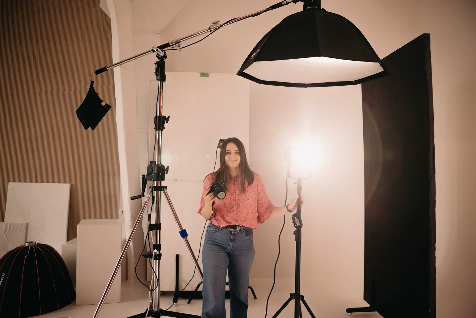 A photographer in a pink shirt under a large beauty dish on a boom, a black flag beside her.