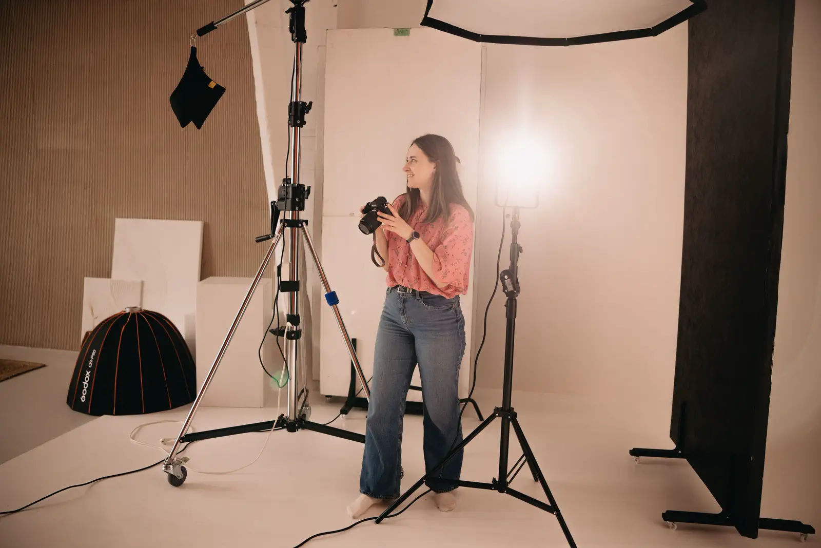 The photographer holding her camera beside a lit stand and a parabolic softbox on the floor.