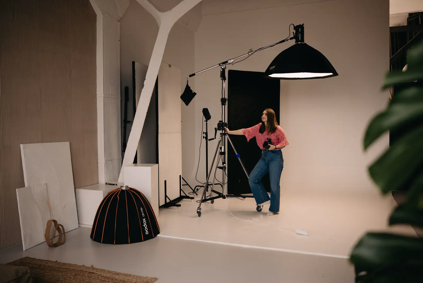 Wide view of the smaller stage: white timber beams, the beauty dish on a boom, the photographer adjusting a stand.