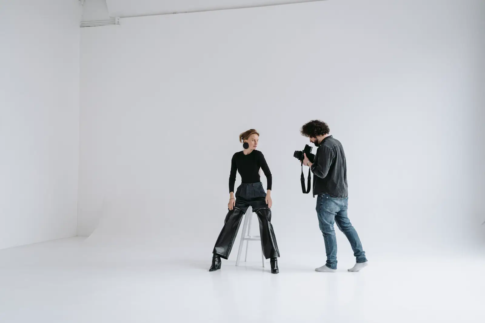 A photographer and a sitter on a stool in the middle of a white cyc studio.