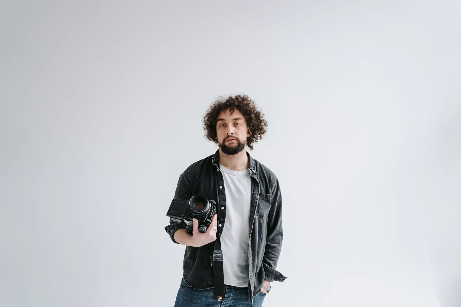 A curly-haired photographer holding his camera in the white studio.