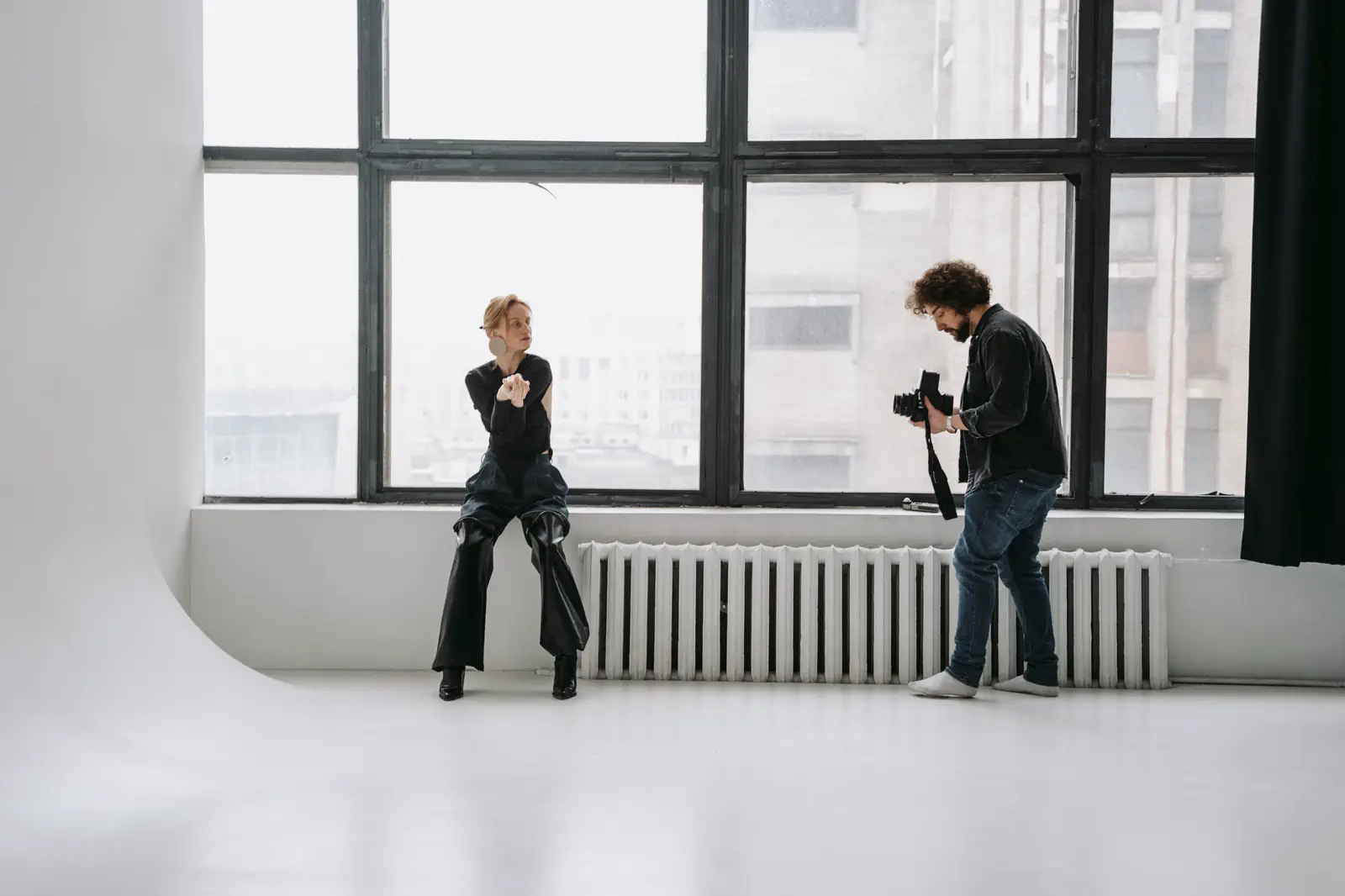 A sitter perched on a radiator under tall industrial windows, the photographer shooting from the floor.