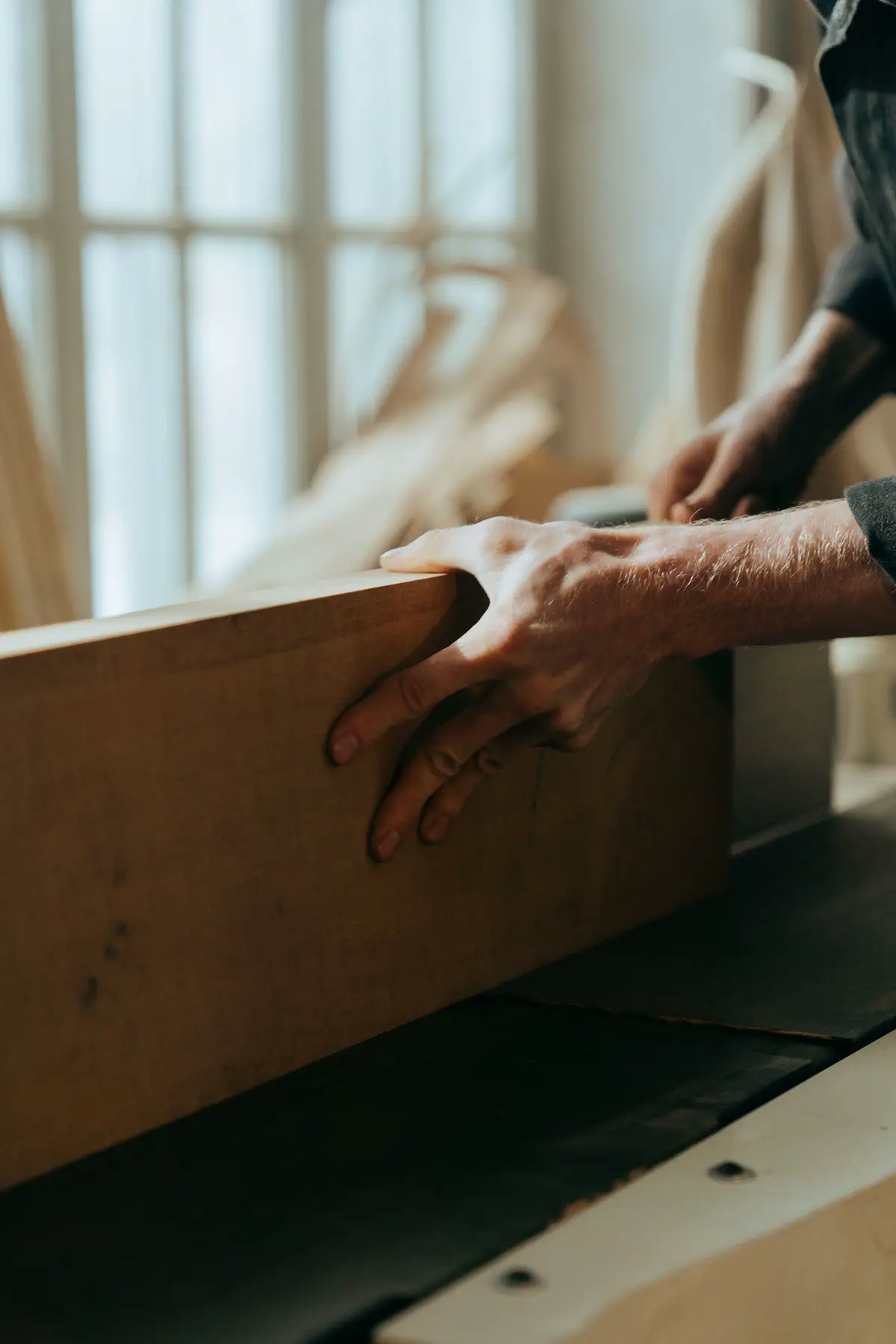 Hands steadying a long board against the window light.