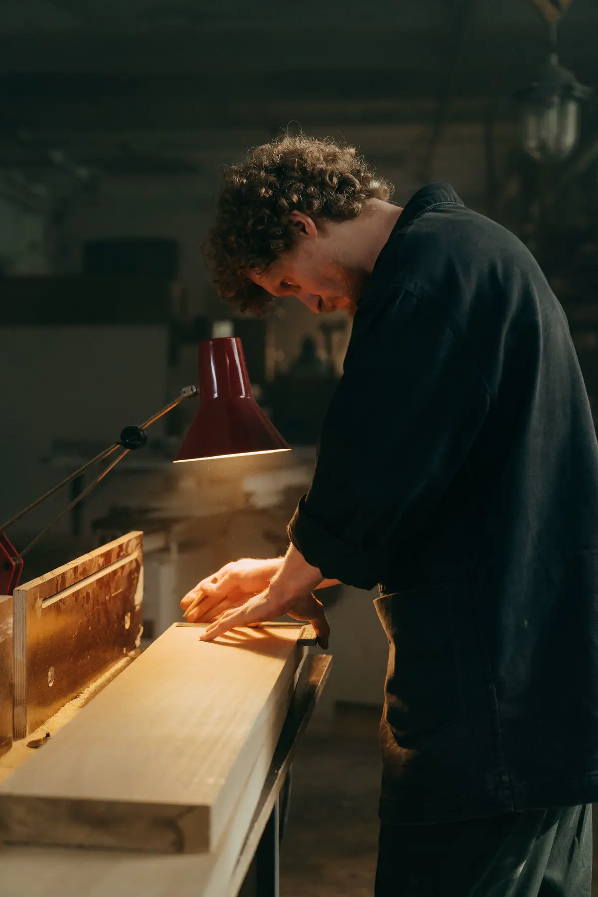The maker leaning over a board under a red desk lamp.