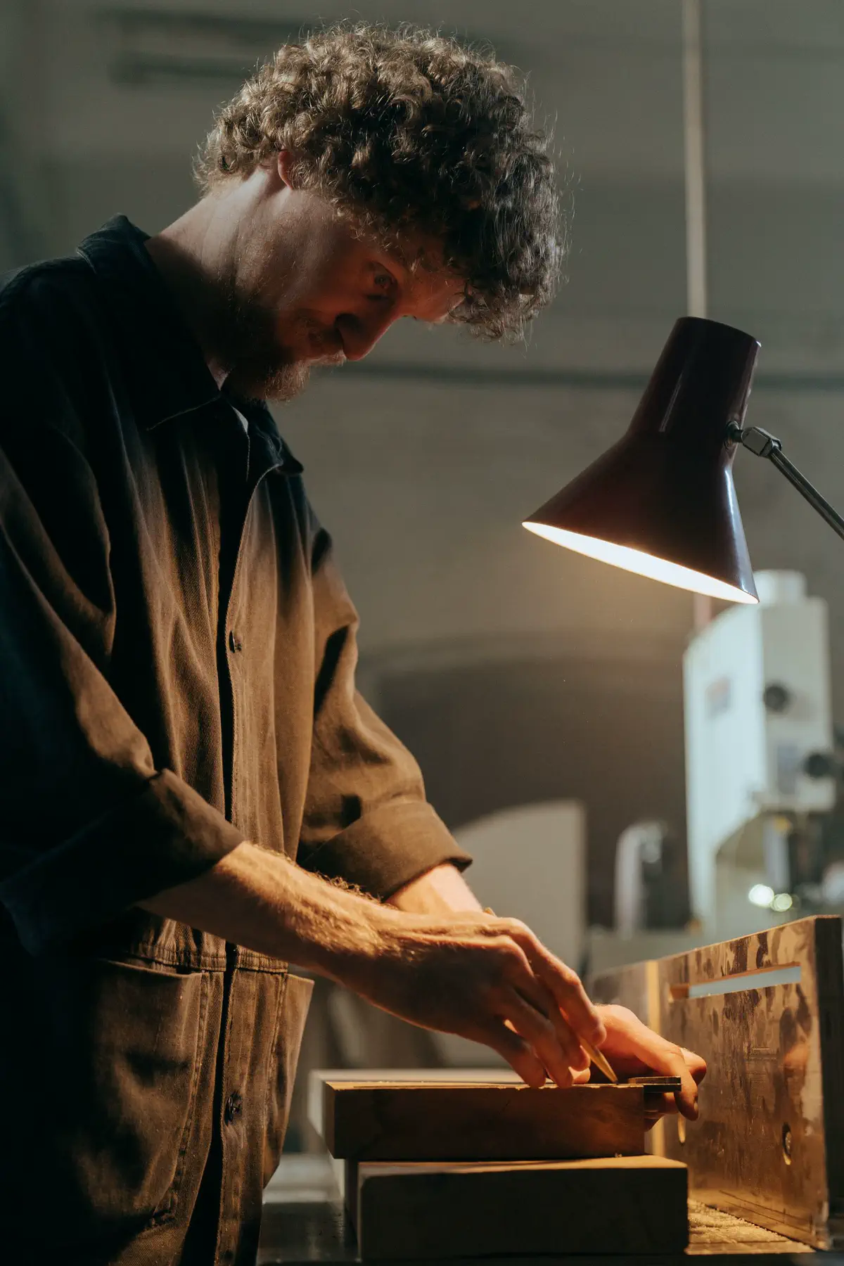 The maker working a small piece at the bench under the lamp.