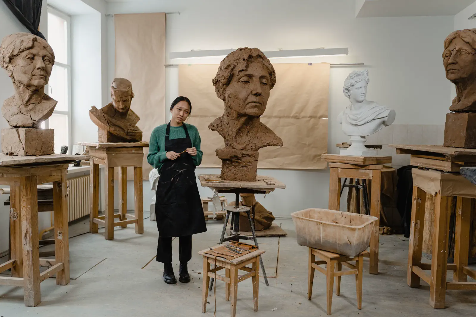 A second sculptor in a green sweater in the studio of clay busts.