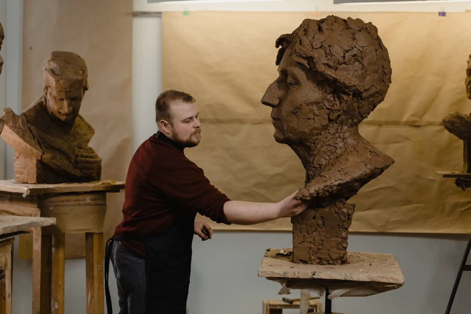 The sculptor modelling the shoulder of the large clay bust.