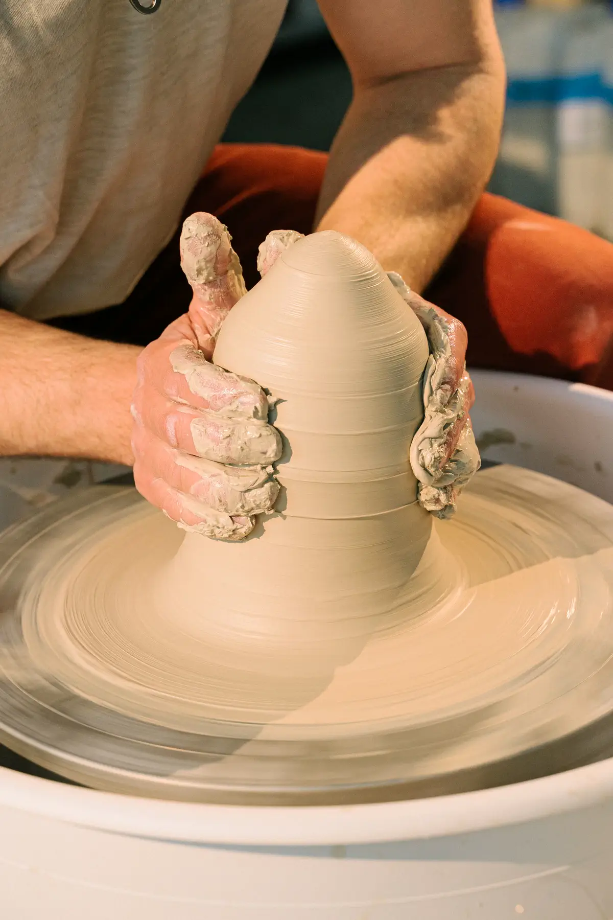 Close view of hands raising the clay on the spinning wheel.