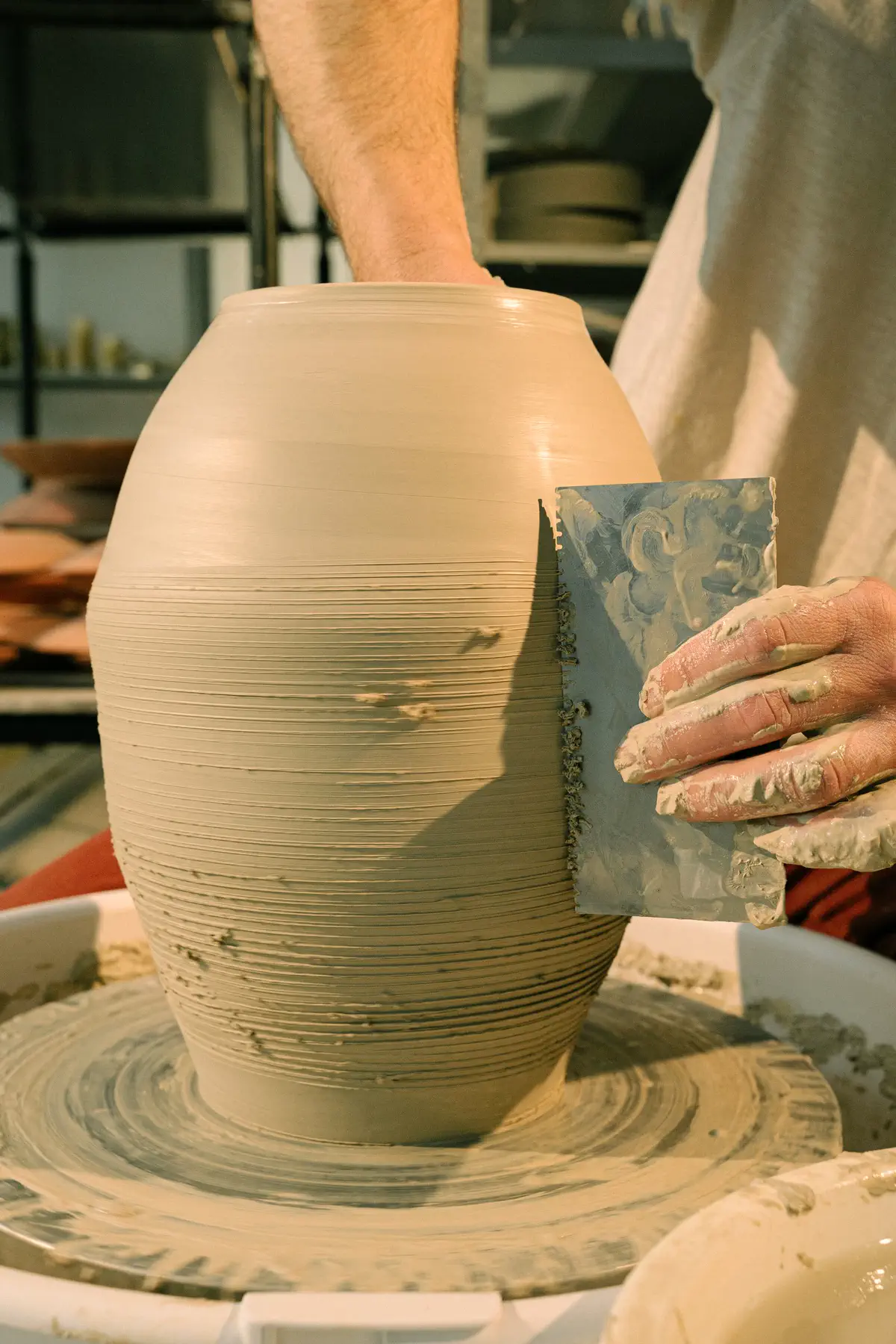 A metal rib scraping the ridged wall of a tall clay vase.
